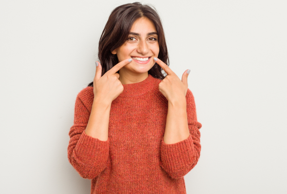 Smiling woman in a red sweater pointing to her straight teeth, showcasing confident results from invisible aligners