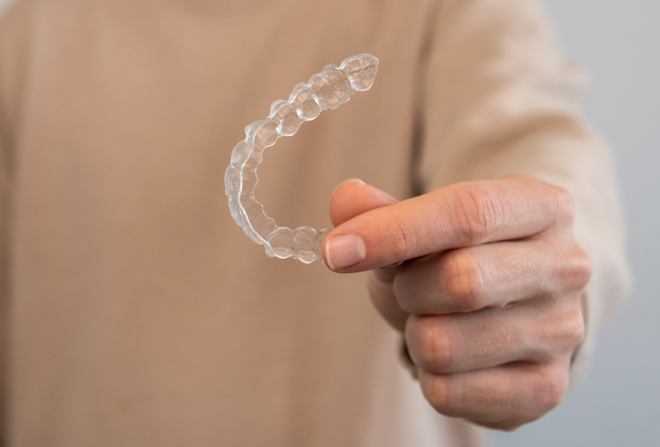 Person holding a clear aligner tray representing the difference between clear aligners and retainers in post-treatment aligner care by Smileie