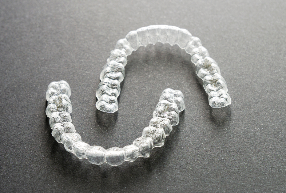 Clear aligner trays placed on a gray surface representing invisible teeth straightening treatment by Smileie
