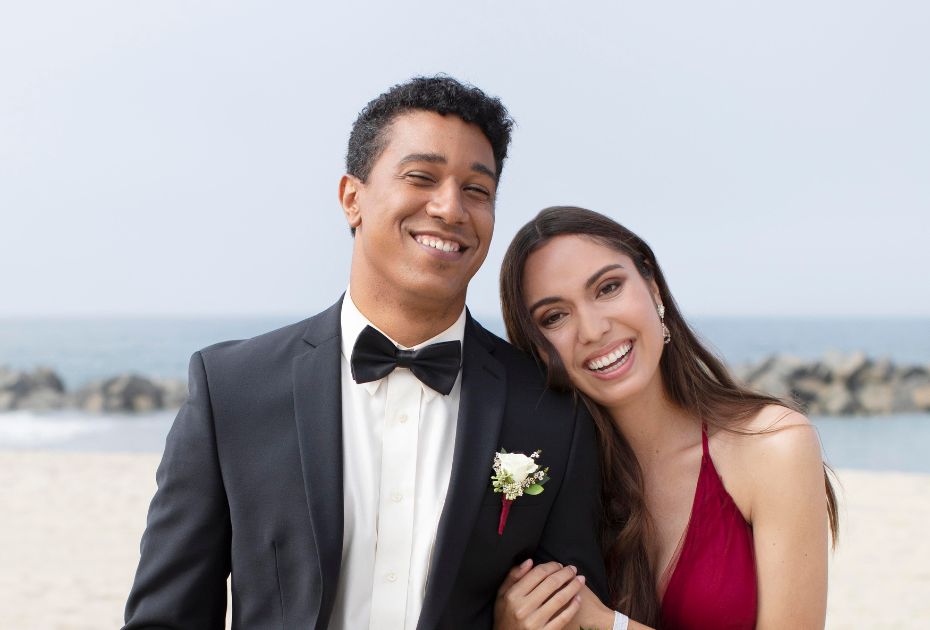 Smiling couple in wedding attire posing on a beach, showcasing confident wedding-ready smiles.