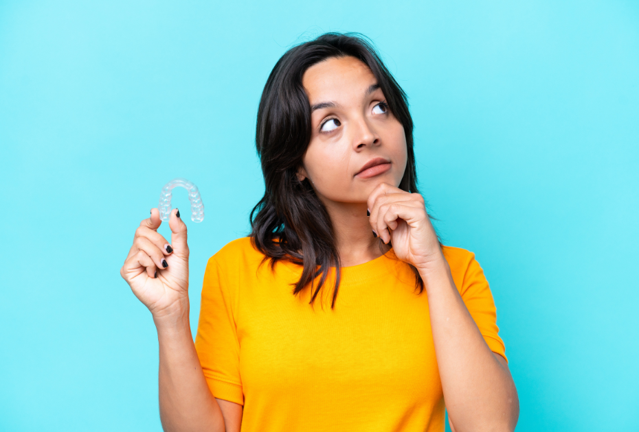 Young woman holding a clear aligner tray and thinking, representing clear aligners for open bite and gaps treatment.