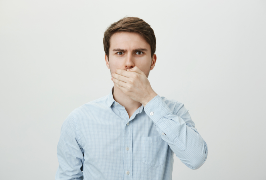Man covering his mouth showing concern about bad breath, concept image for clear aligner hygiene and fresh breath solutions.