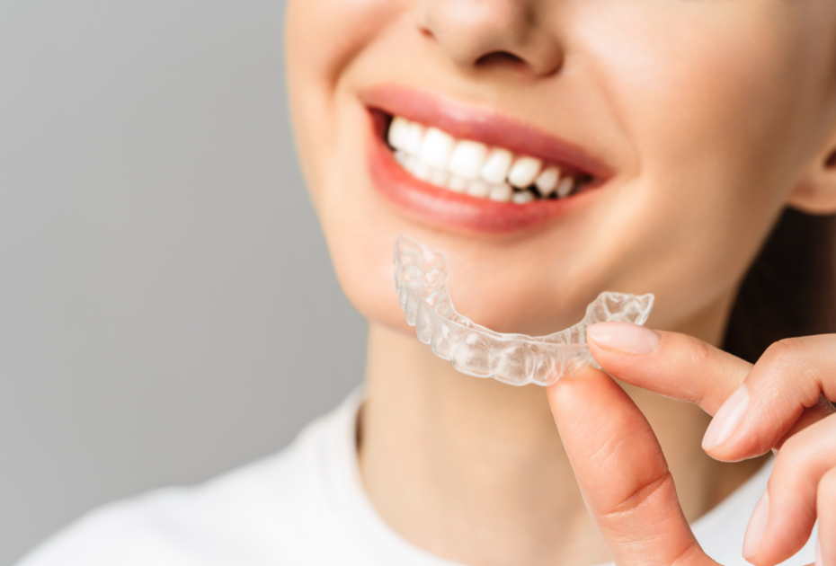 Close-up of a smiling woman holding a clear dental aligner tray near her mouth.