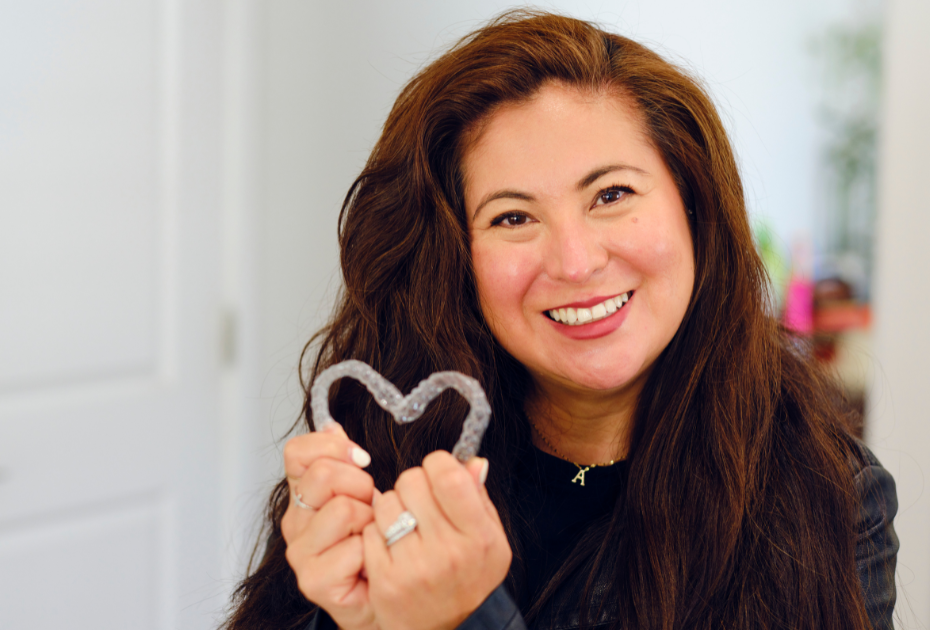 Smiling woman holding clear aligners shaped like a heart, representing a confident smile journey with clear aligners.