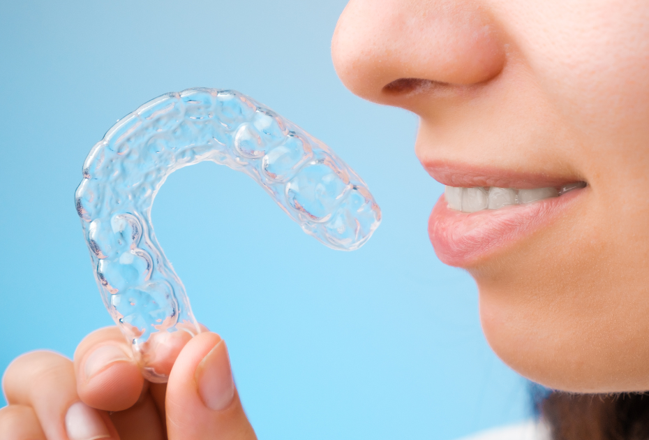 Clear aligner being held near a smiling mouth, illustrating modern clear aligner treatment for teeth spacing and crowding correction