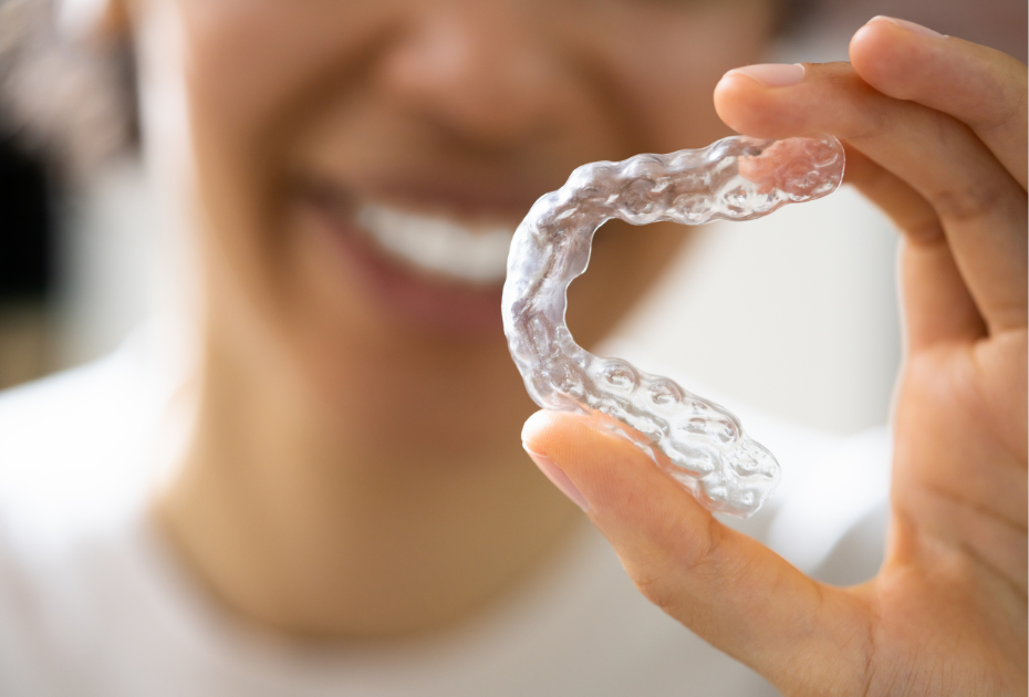 Smiling person holding a clear aligner tray designed for upper or lower teeth correction.