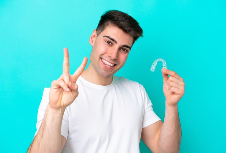 Smiling young man holding a clear aligner tray, representing clear aligners for adults.