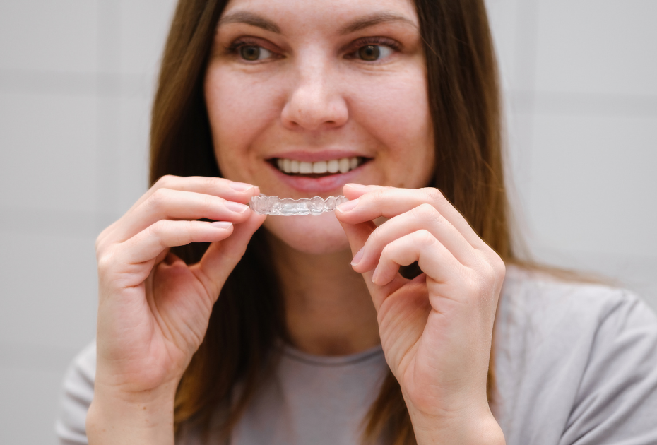 Woman checking her smile in the mirror while holding clear aligners.
