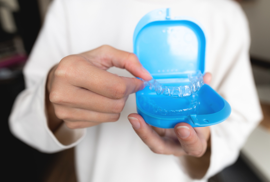 Person holding clear aligners and placing them into a blue aligner case as part of a clear aligner travel kit routine.