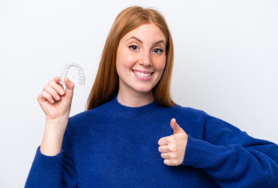 Woman holding clear aligner and smiling, showing cost-effective invisible teeth straightening option in the USA.