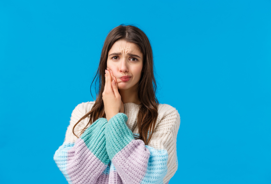 Young woman with tooth pain showing signs of teeth sensitivity on blue background