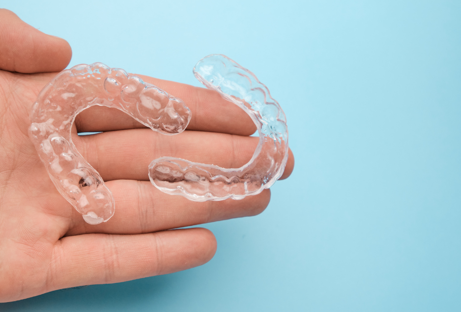 Hand holding two clear dental retainers on a blue background – night vs day retainer comparison