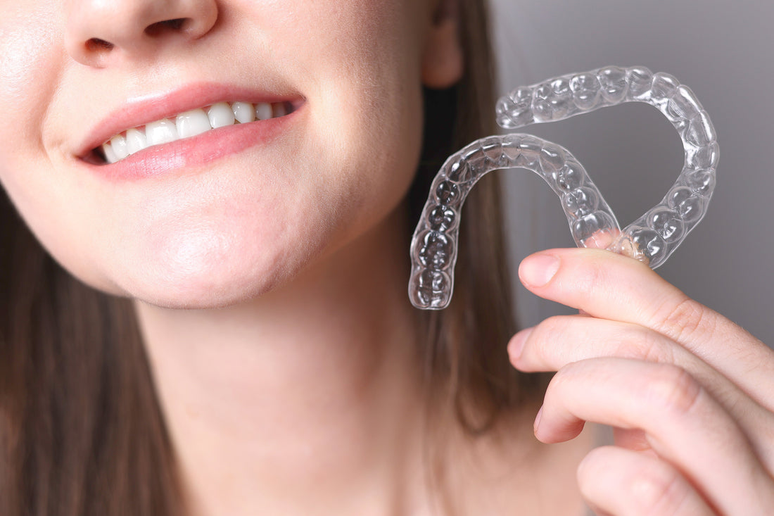 Woman holding a pair of clear aligners before starting teeth straightening treatment.